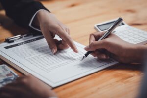 Close-up of hands signing a contract on a wooden desk, with a pen, a calculator